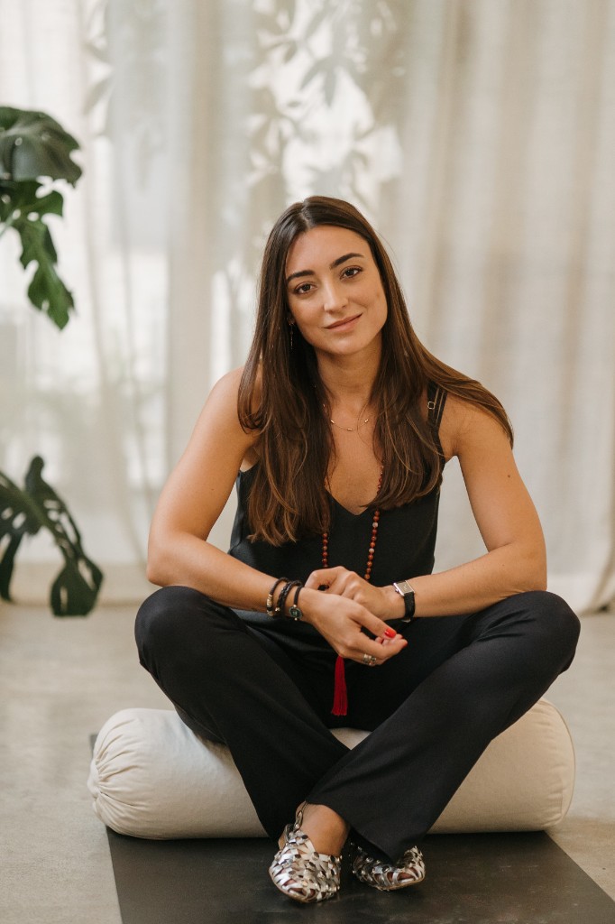 Júlia Sans seated cross-legged, hands clasped, looking toward the camera.
