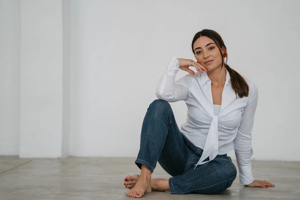 Júlia Sans in a white studio, seated on the floor with one knee raised.